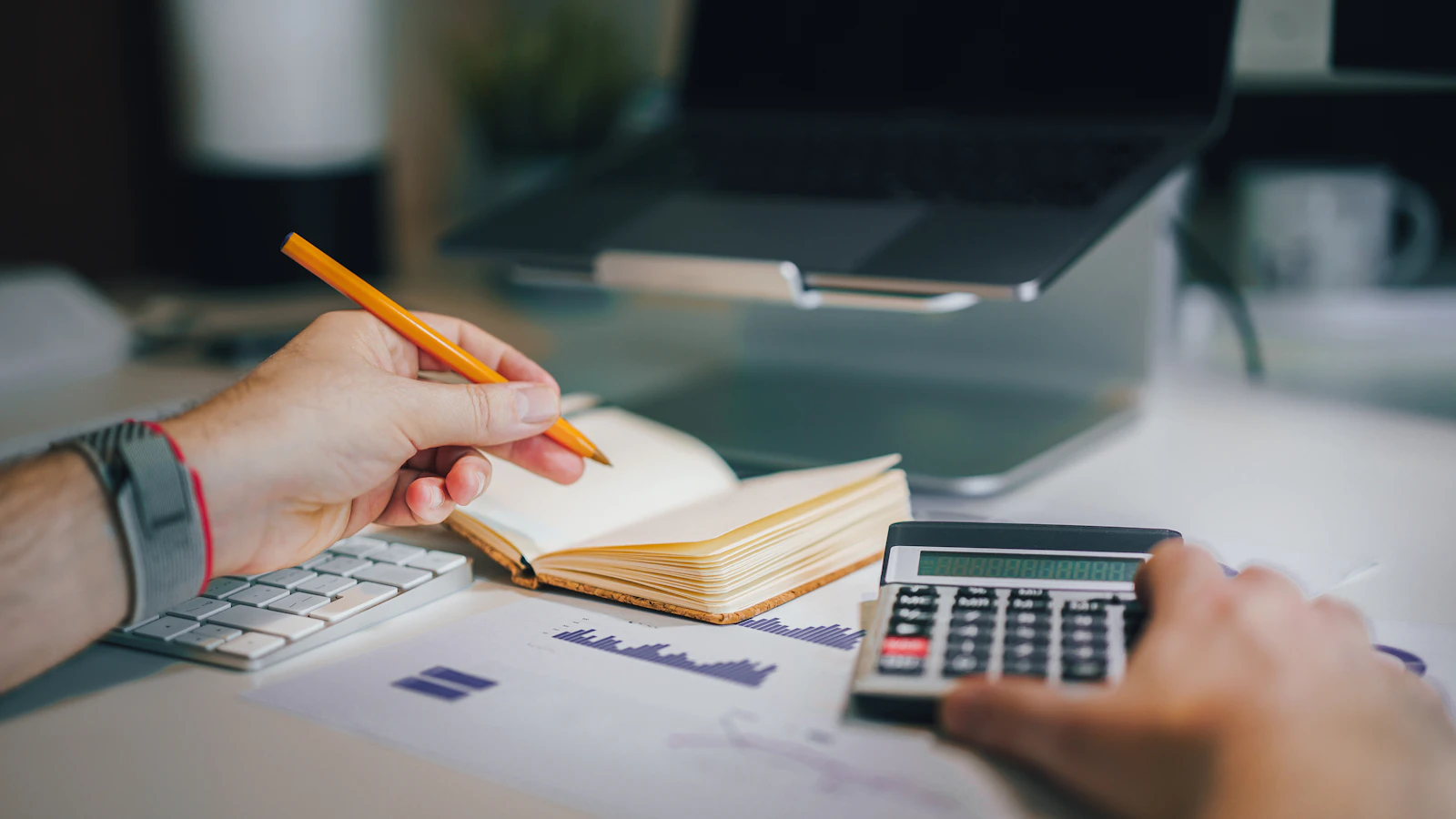 Personne écrivant dans un cahier à côté d'une calculatrice et de documents de travail